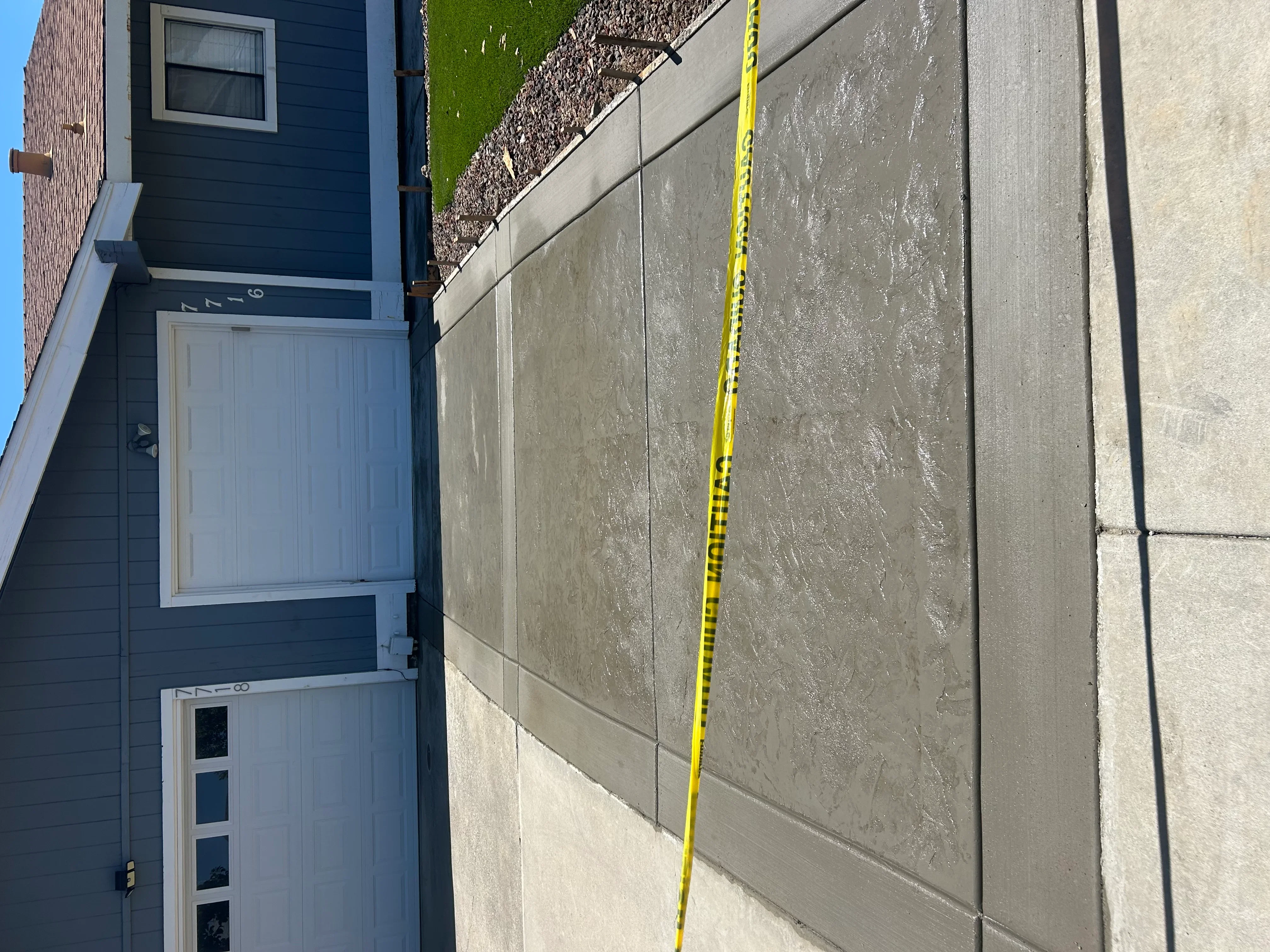Newly installed concrete driveway with control joints and yellow measuring tape