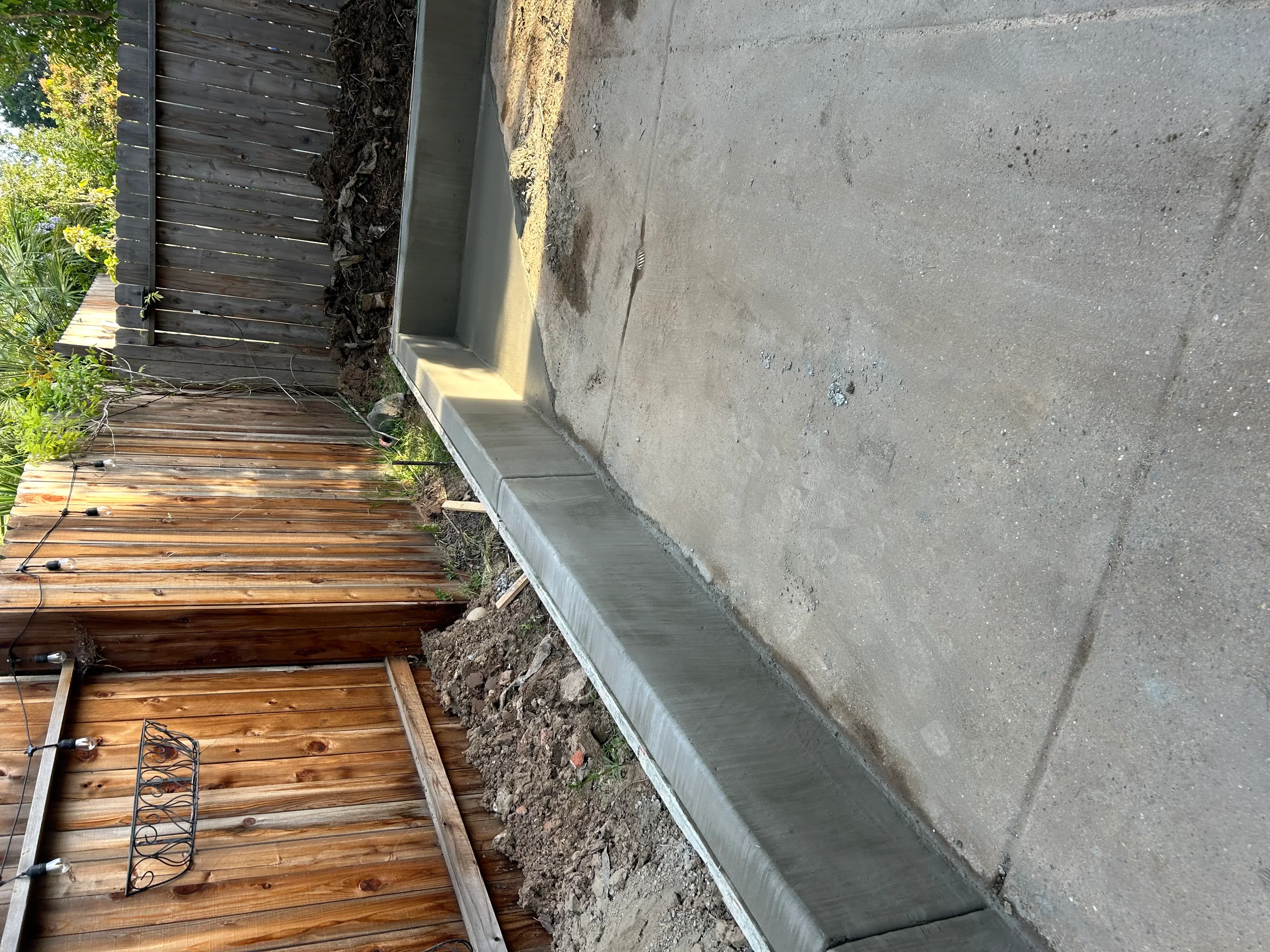 Concrete foundation apron with aluminum trim installed next to wooden deck framing