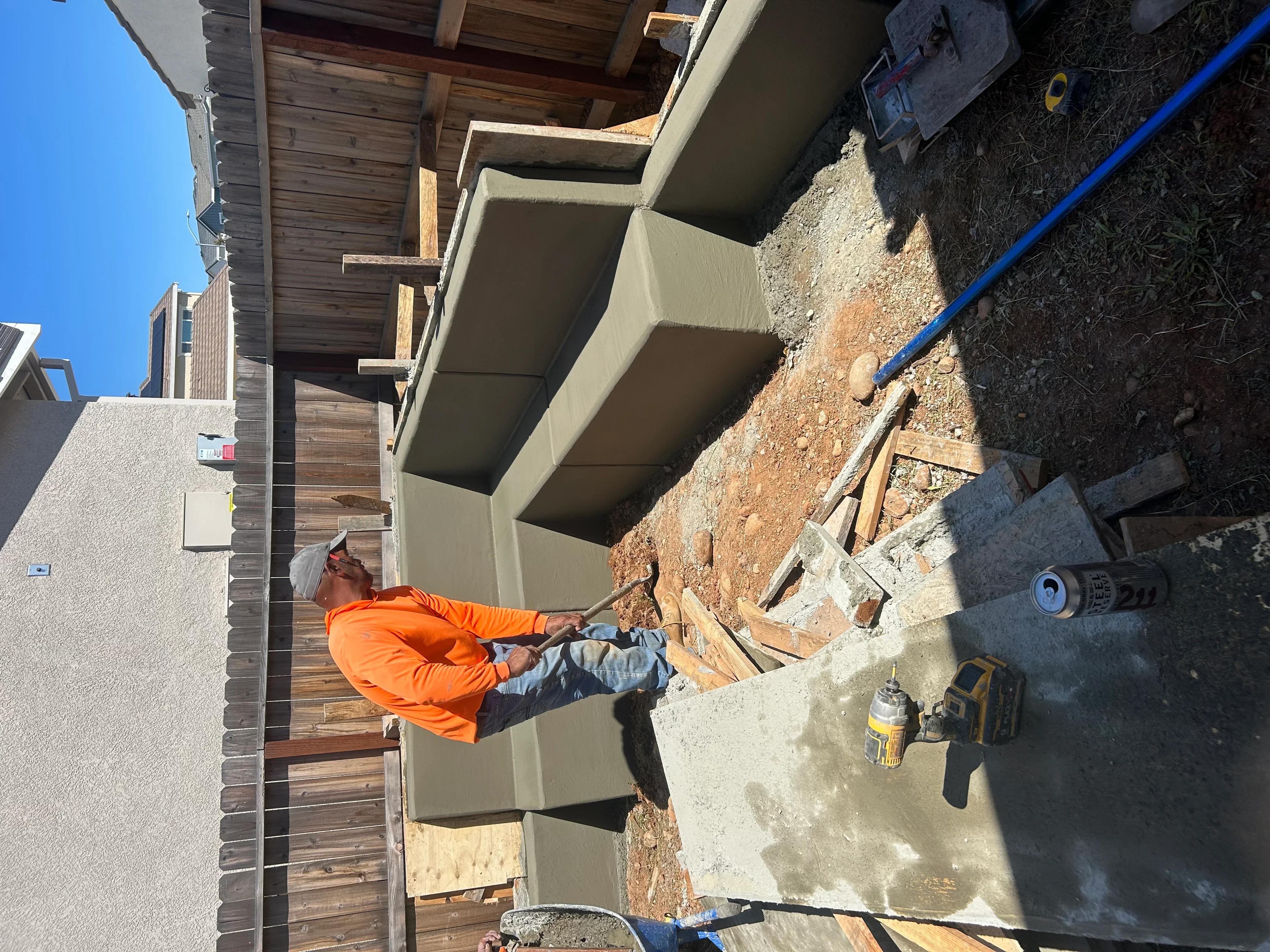 Worker in orange jacket installing concrete foundation elements on residential construction site
