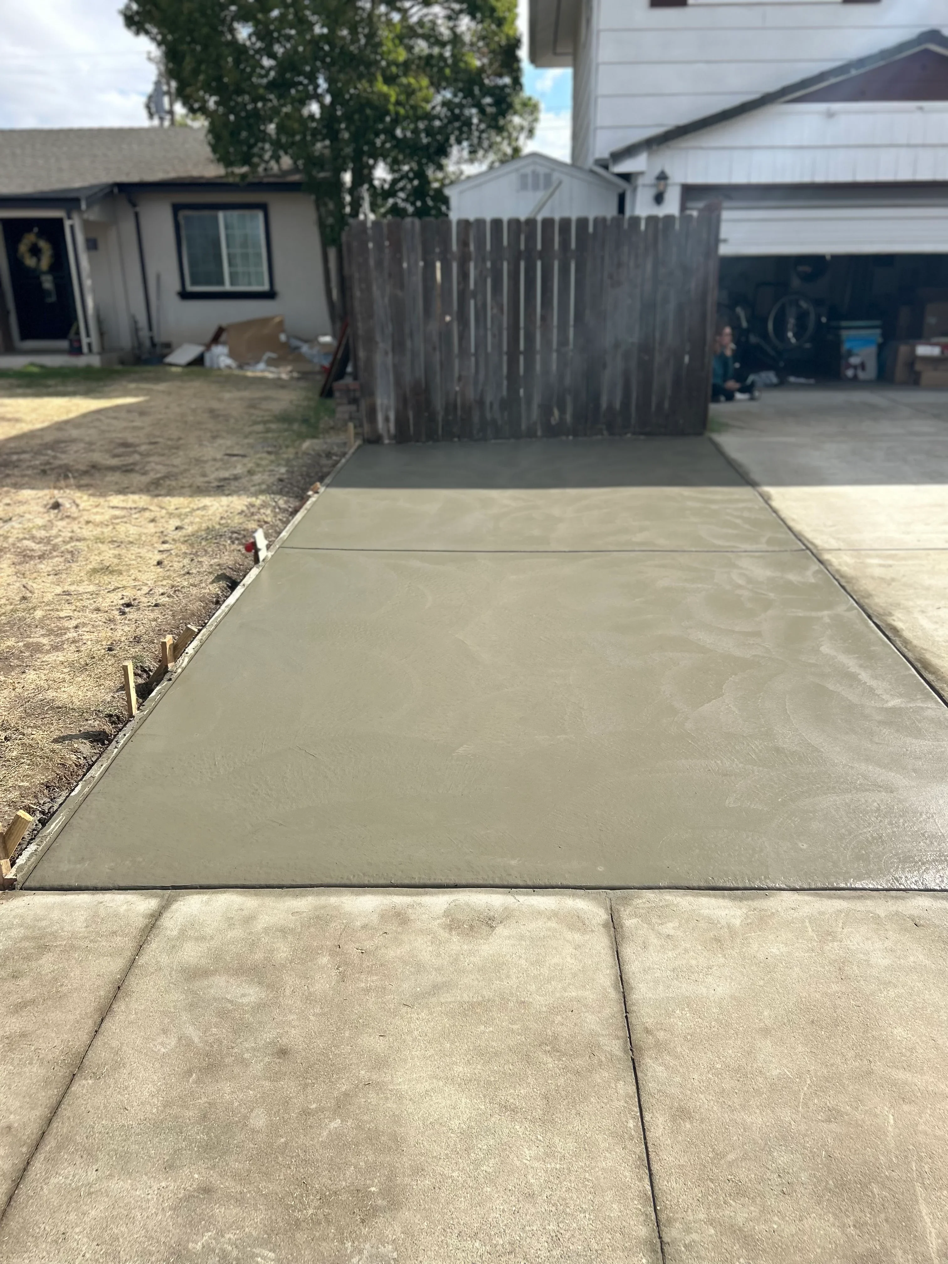 Newly poured concrete driveway extension with metal edging and smooth finish
