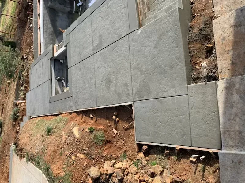 Gray concrete foundation panels installed on hillside excavation with exposed soil and grading work