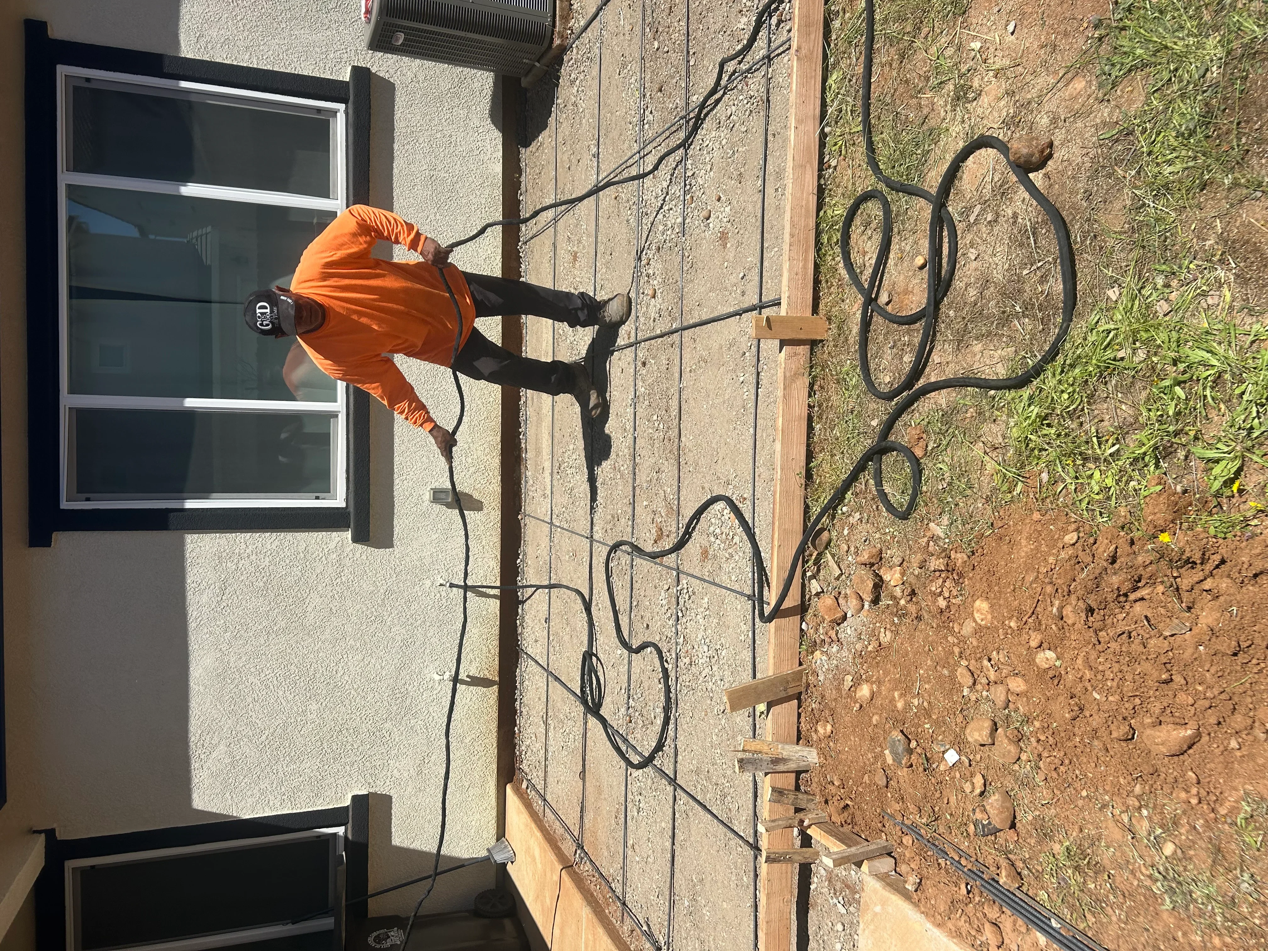 Worker in orange shirt installing concrete foundation with steel rebar and wooden forms on sloped site